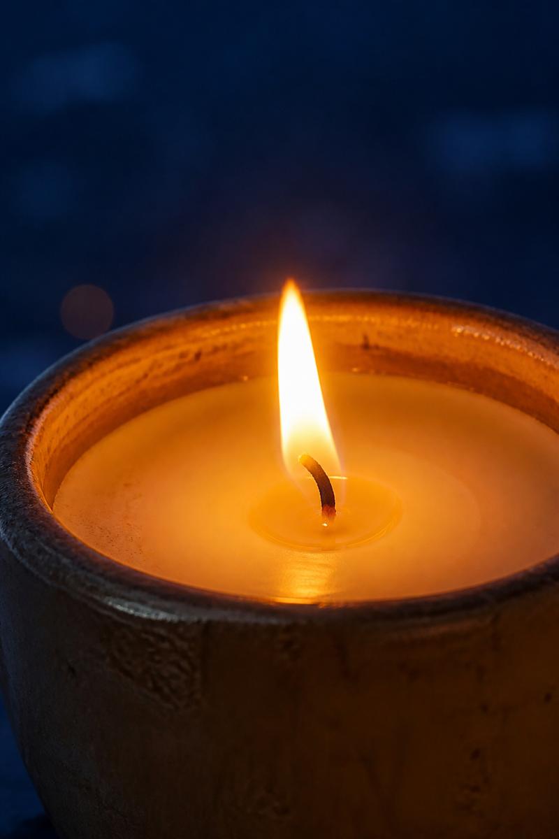 Lit candle flame in a ceramic vessel with warm glow